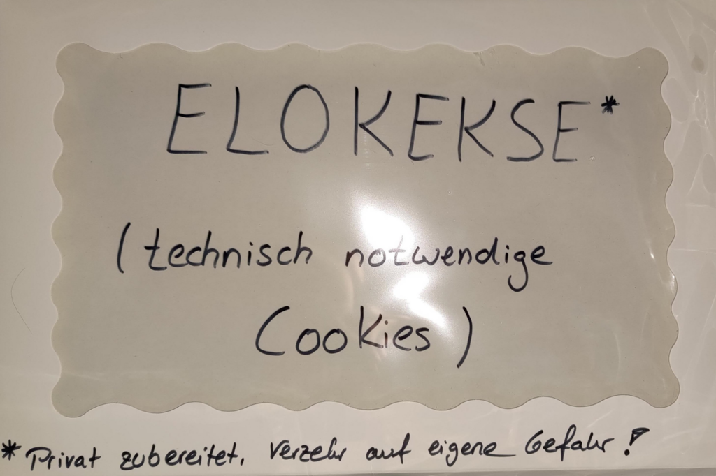 Handgeschriebenes Schild mit der Aufschrift „ELOKEKSE* (technisch notwendige Cookies)“ – darunter ein Hinweis: „*Privat zubereitet. Verzehr auf eigene Gefahr!“ – humorvoll inszenierte Büroküche bei eloquium.